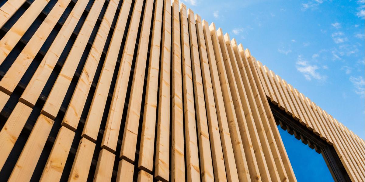 Holzfassade mit vertikalen Lamellen, modernes Design vor blauem Himmel mit leichten Wolken, Architekturdetail.