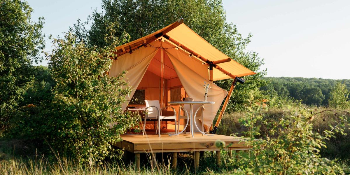 Gelbes Glamping-Zelt auf Holzplattform, umgeben von Büschen.