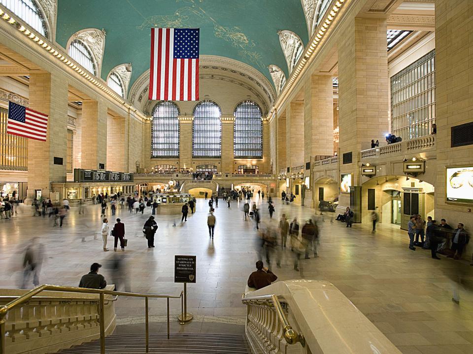 Grand Central Terminal in New York mit hoher Decke, amerikanischer Flagge und geschäftigem Treiben der Reisenden____