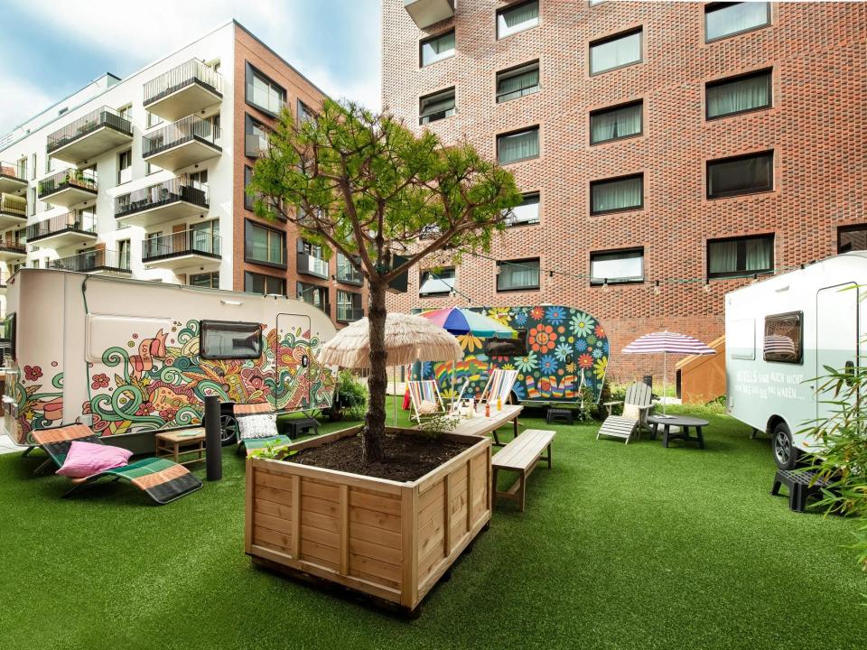 Bunte Wohnwagen und Sitzmöglichkeiten auf einer begrünten Dachterrasse.____