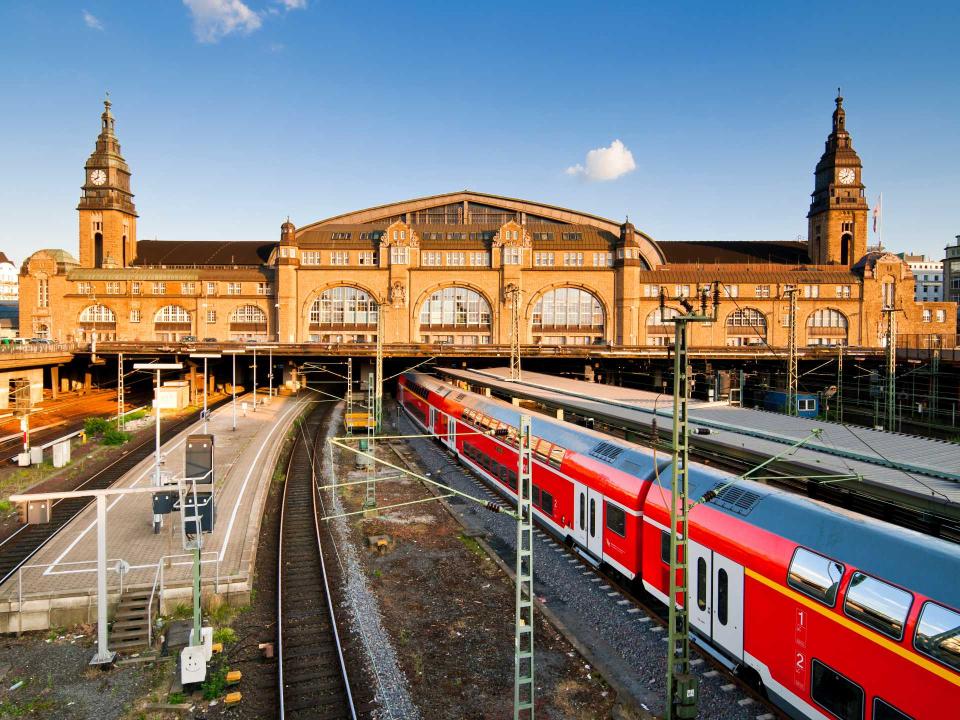 Außenansicht des Hamburger Hauptbahnhofs mit rotem Regionalzug und beeindruckender historischer Architektur bei Sonnenuntergang____