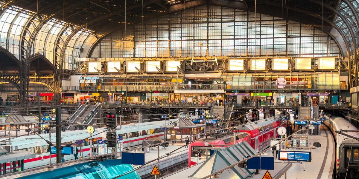 Innenansicht des Hamburger Hauptbahnhofs mit roten und blauen Zügen, Gleisanlagen und heller Bahnhofshalle