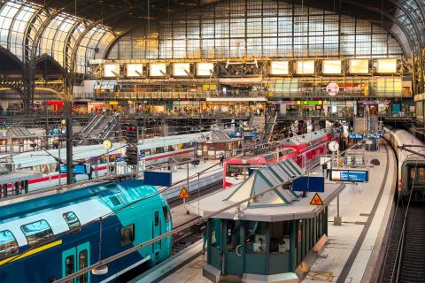 Innenansicht des Hamburger Hauptbahnhofs mit roten und blauen Zügen, Gleisanlagen und heller Bahnhofshalle