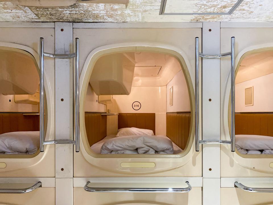 Innenansicht einer klassischen Kapselhotel-Schlafkabine mit einem weißen Bett und hölzernen Wandverkleidungen____
