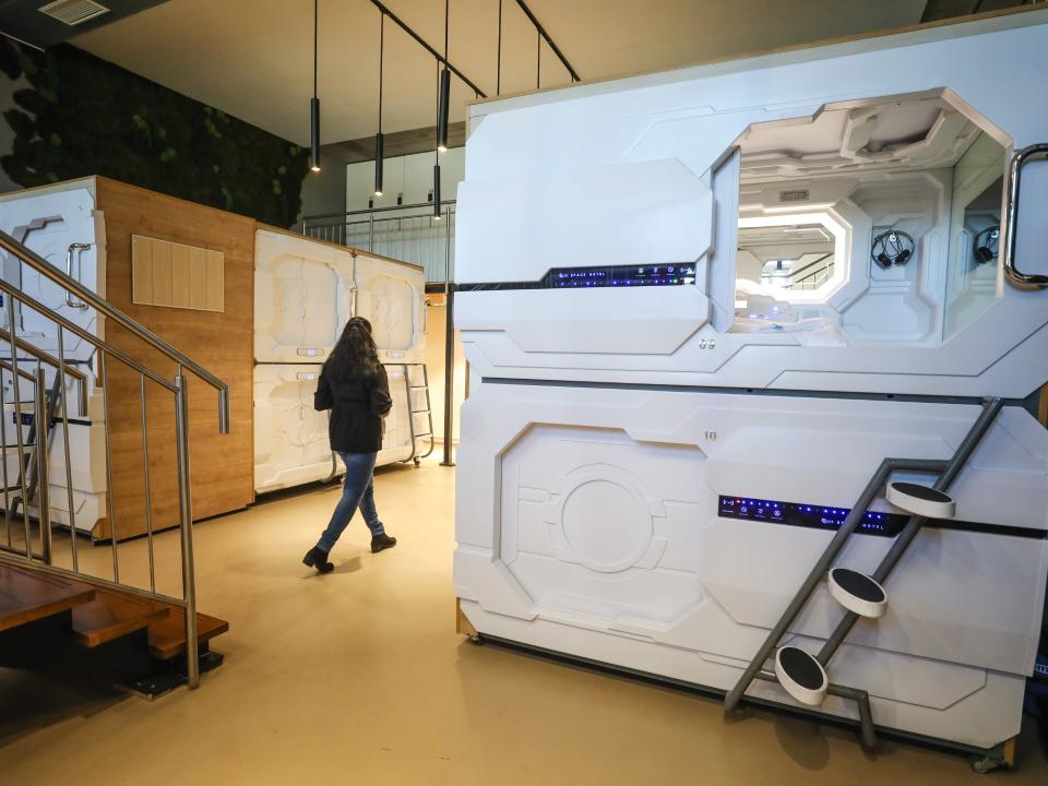 Futuristische Kapselhotel-Einheiten mit weißem Hightech-Design und LED-Panels, Treppe für obere Kabine sichtbar____