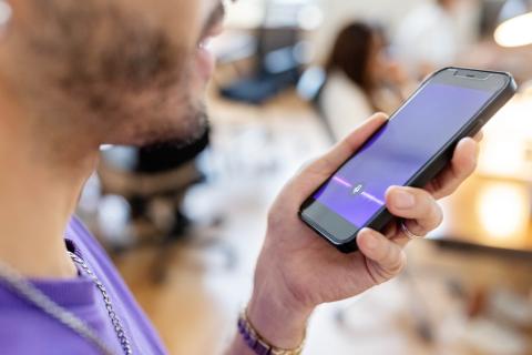 Mann spricht in Smartphone mit aktivierter Sprach-KI-App, Fokus auf Display mit bunter Audio-Wellenanzeige.
