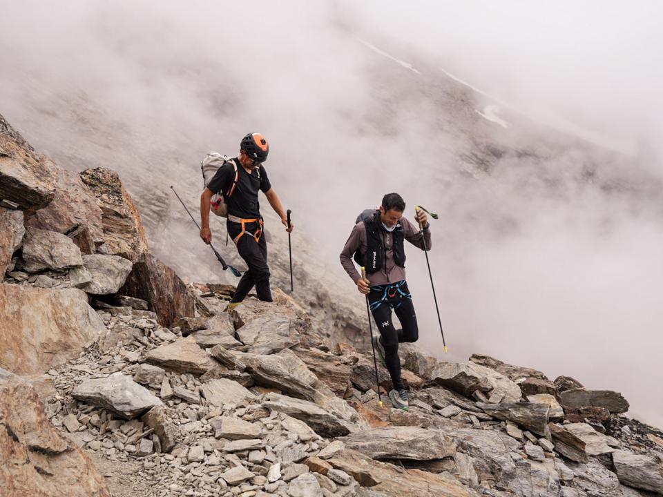 Zwei Bergsteiger navigieren auf felsigem Gelände im Nebel.____