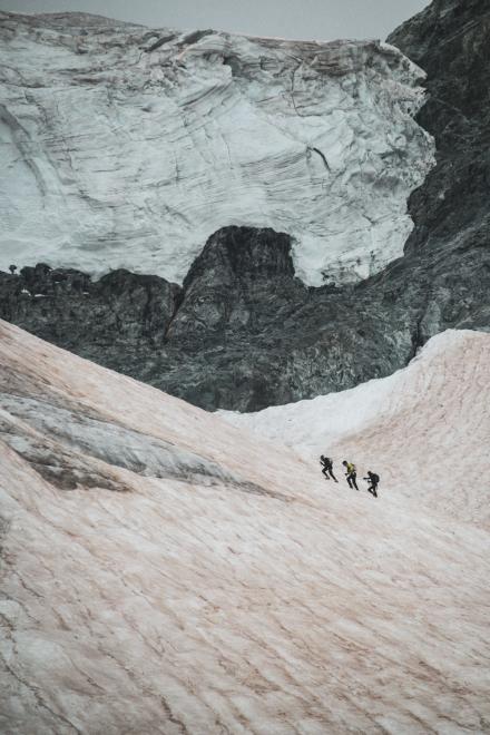 Drei Kletterer überqueren einen schneebedeckten Hang vor einer Gletscherwand.