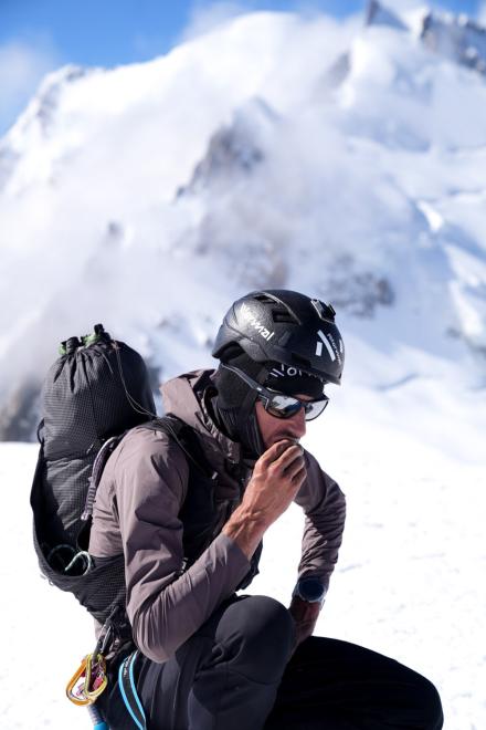 Bergsteiger macht Pause im Schnee, isst und trägt einen schwarzen Helm.