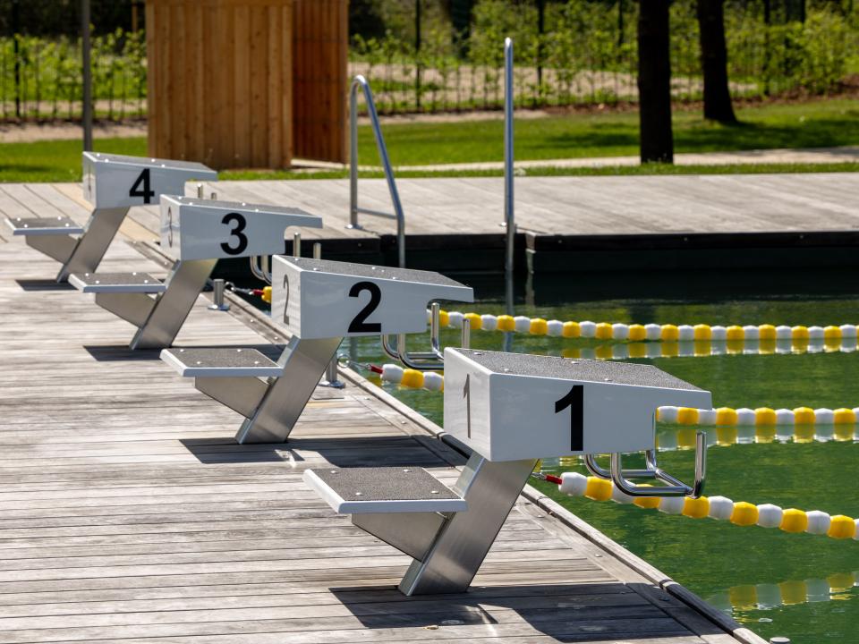 Startblöcke am Rand eines Schwimmbeckens mit gelb-weißen Leinen, nummeriert von 1 bis 4 auf Holzsteg.____