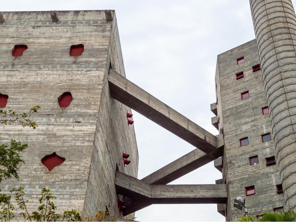 Brutalistisches Betongebäude mit roten Fensterakzenten und Verbindungselementen zwischen den Blöcken.____
