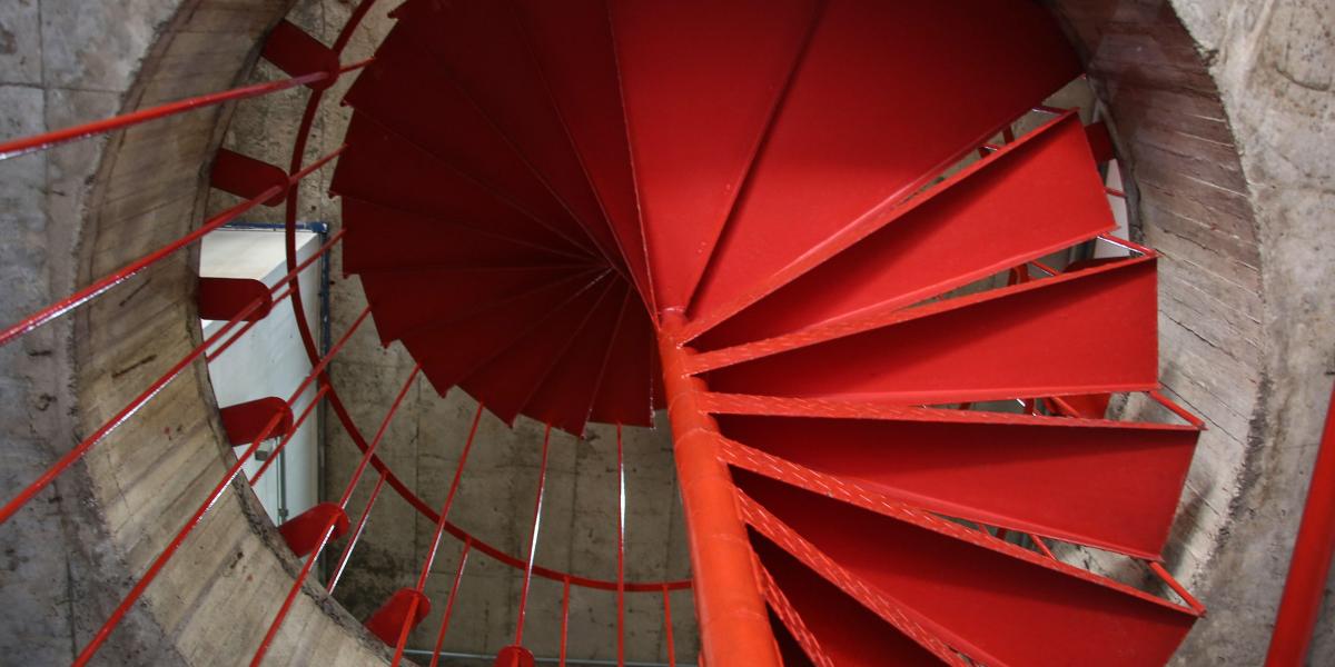 Rote Wendeltreppe aus Metall in einem Betongebäude, von oben nach unten fotografiert.
