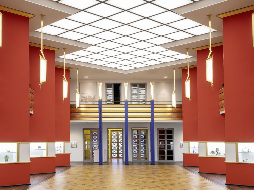 Helles, modern gestaltetes Museum mit roten Wänden, beleuchteten Vitrinen und einer geometrischen Deckenbeleuchtung____