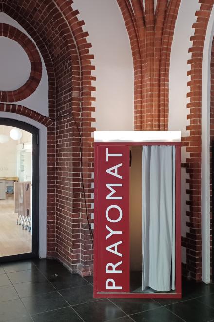 Roter "Prayomat"-Automat in einem modernen Innenraum mit Backsteinwänden, der eine Gebetseinrichtung anbietet