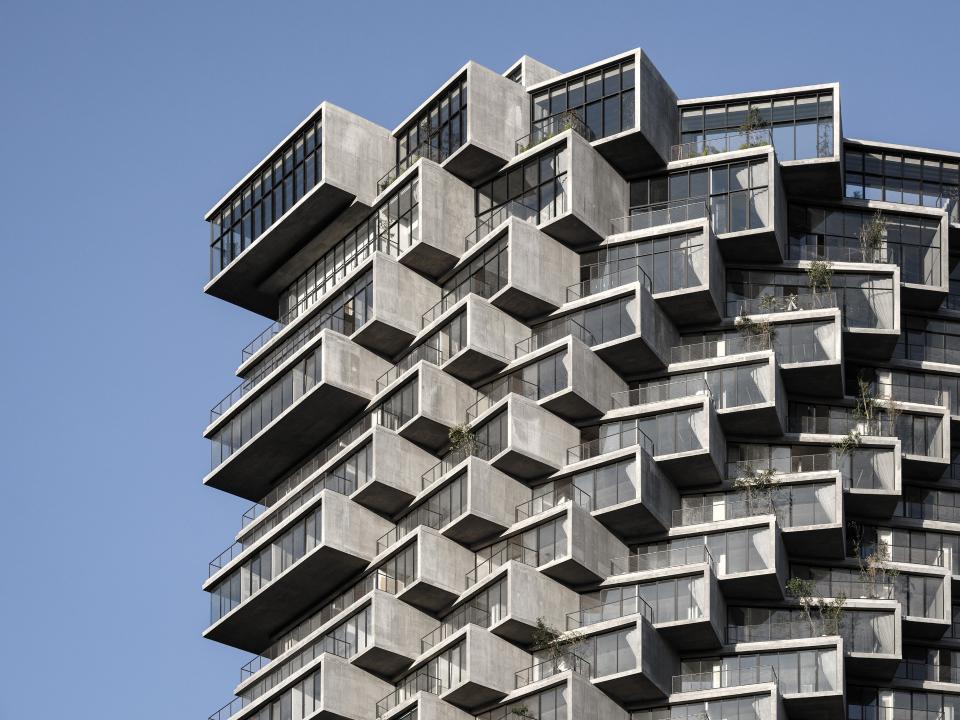 Modernes Hochhaus mit versetzten Balkonen und großen Glasfenstern.____