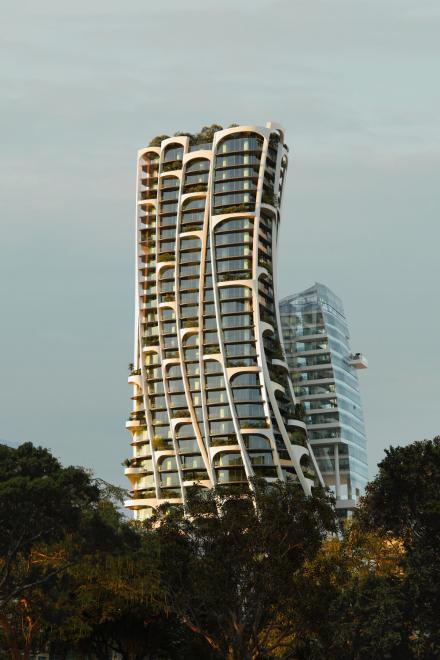 Geschwungenes Hochhaus mit begrünten Balkonen und weißer Fassade.