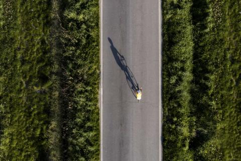 Luftaufnahme eines allein fahrenden Radfahrers mit gelbem Trikot auf gerader Straße durch grüne Landschaft