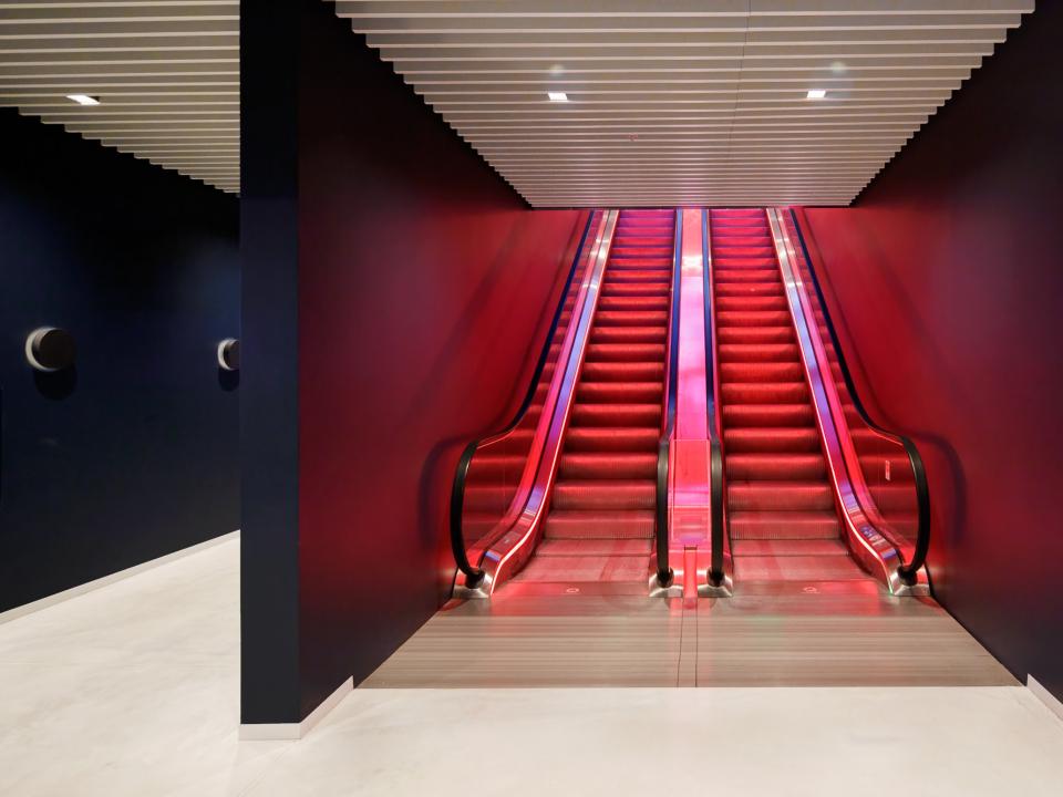 Rote Schindler Rolltreppen in futuristischer Halle mit dunklen Wänden und hellem Boden.____