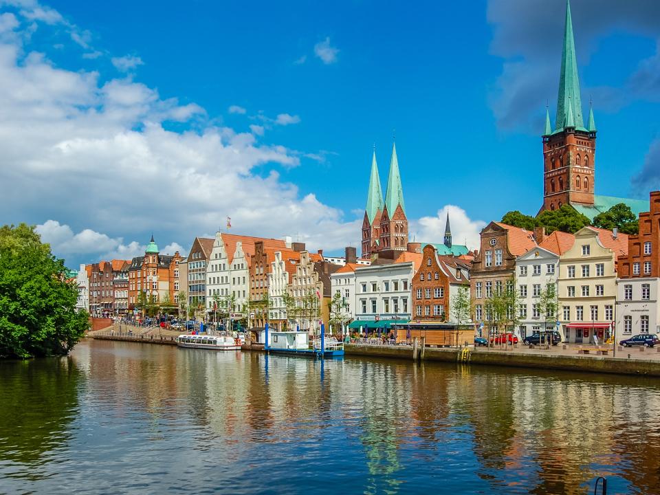 Lübecks Altstadt mit historischen Gebäuden und Kirchen, reflektiert im Wasser der Trave bei blauem Himmel.____
