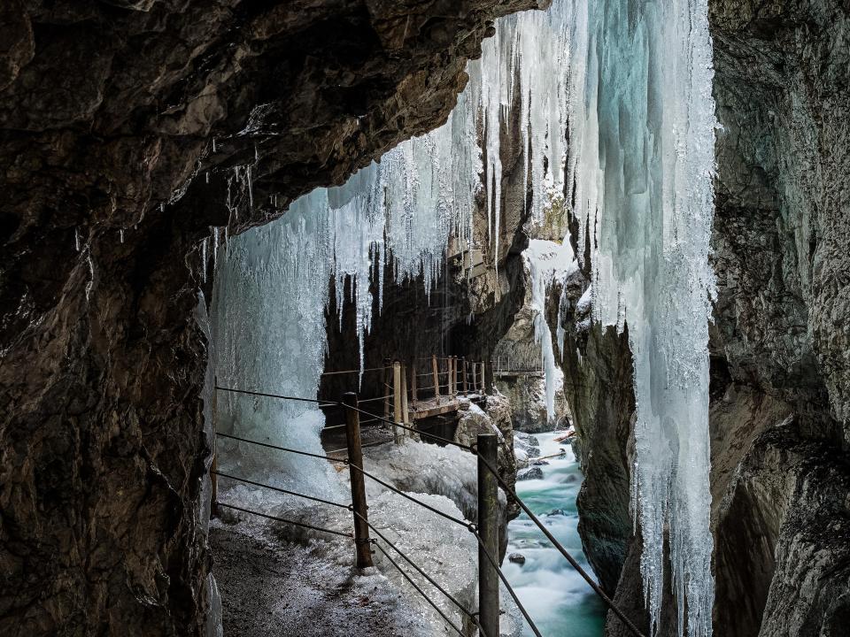 Eishöhle mit großen gefrorenen Stalaktiten und eisbedecktem Fluss.____