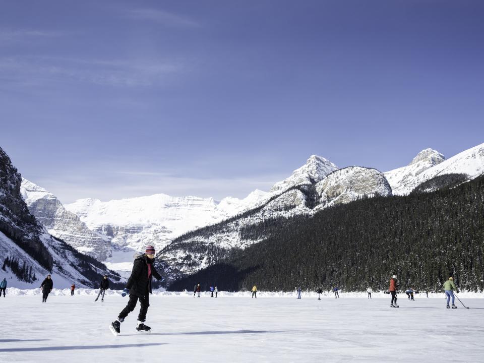 Menschen beim Schlittschuhlaufen auf einem zugefrorenen See, umgeben von verschneiten Bergen.____