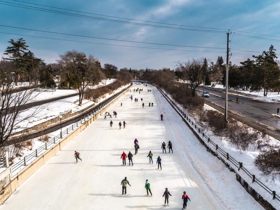 Schlittschuhläufer auf einem gefrorenen Kanal mit schneebedeckter Landschaft und Bäumen.____