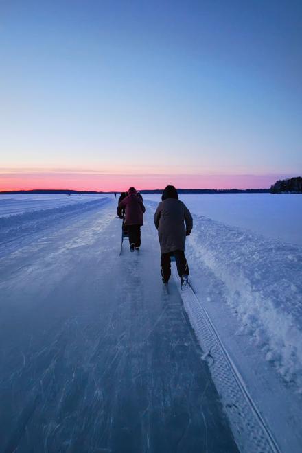 Zwei Personen laufen auf einer zugefrorenen Bahn im Sonnenuntergang, umgeben von schneebedeckter Landschaft.