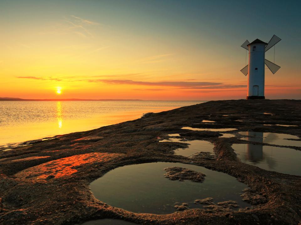 Weißer Leuchtturm bei Sonnenuntergang auf felsiger Küste mit Wasserpfützen.____
