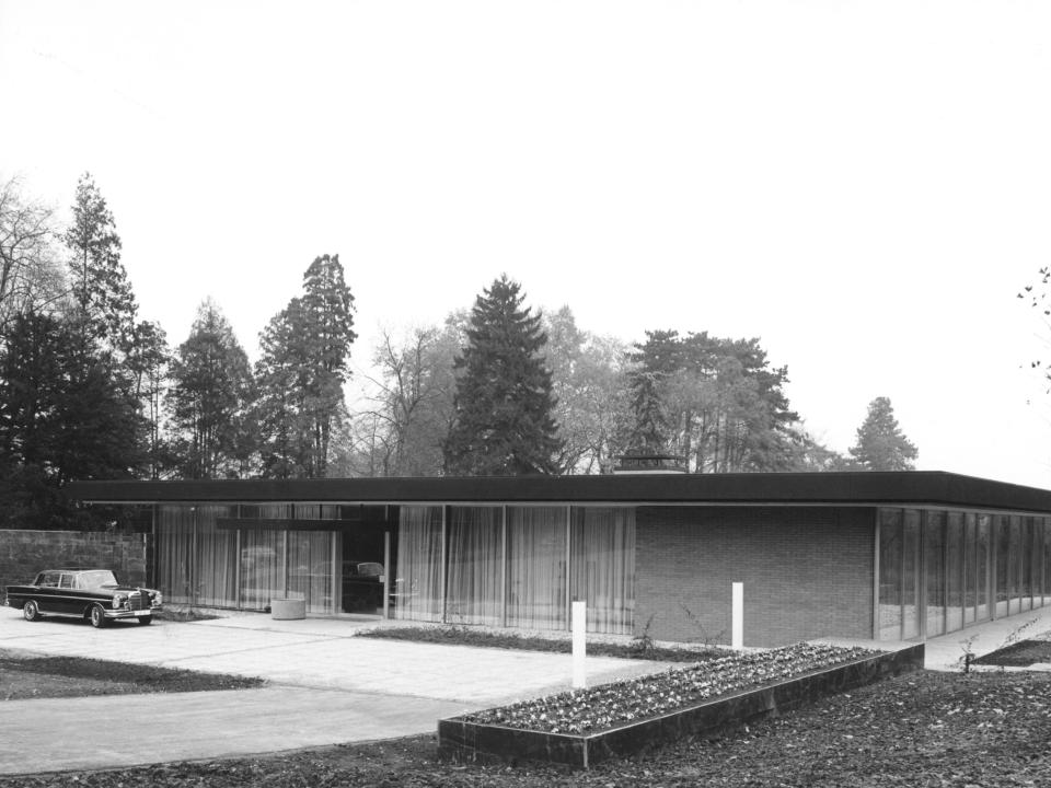 Flach gebautes Haus mit Glasfassade und Vordach, davor ein klassischer Mercedes und gepflegte Einfahrt.____