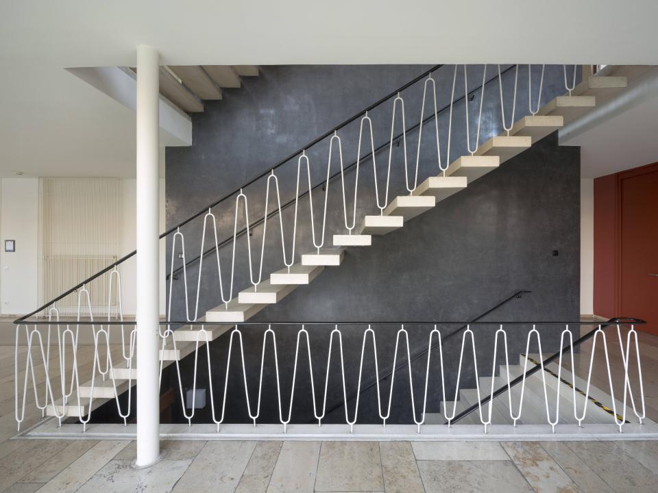 Schwebende Betontreppe mit geschwungenem weißem Geländer vor dunkler Wand im modernen Treppenhaus.____