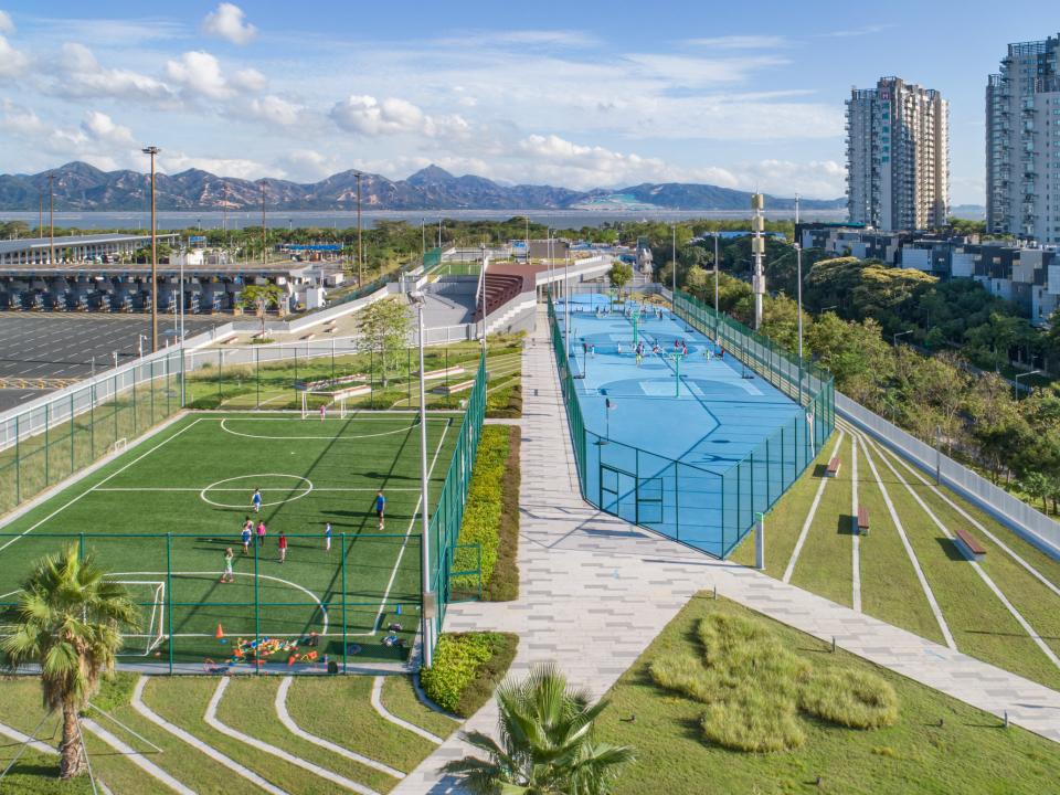 Park mit Fußballplatz und Basketballplatz vor den Bergen und Stadtgebäuden.____