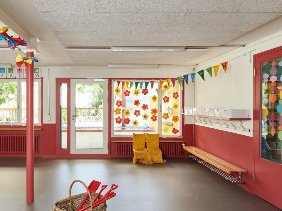 Heller Kindergartenraum mit bunten Blumenaufklebern an den Fenstern und Wimpelgirlande.____