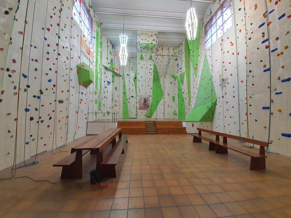Kletterhalle mit hohen Wänden und bunten Griffen, Bänke im Vordergrund.____