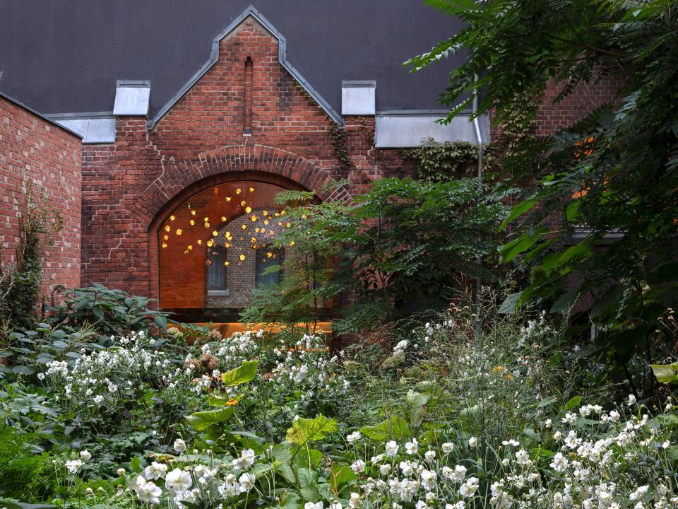 Üppiger Garten vor roter Backsteinfassade mit beleuchteten Fenstern.____