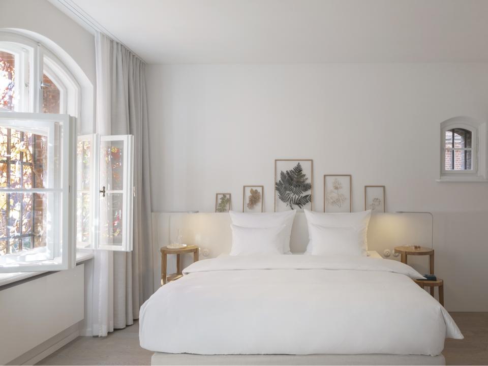 Helles Schlafzimmer mit weißen Bettwäsche und offenen Fenstern.____