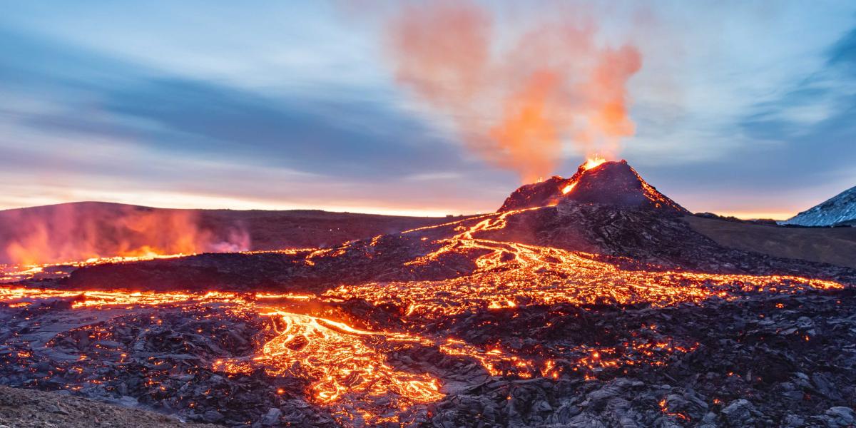 Luftaufnahme eines Vulkanausbruchs mit leuchtender Lava, die aus dem Krater fließt, und aufsteigendem Rauch