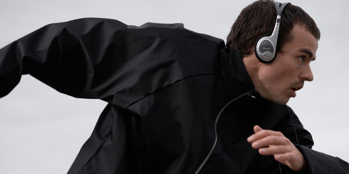 Sportlicher Mann in schwarzer Jacke läuft mit Kopfhörern, Bewegung und Entschlossenheit sichtbar.