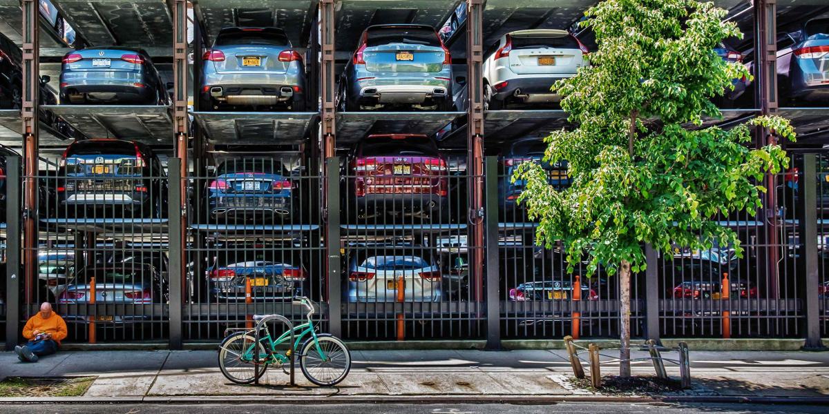 Vertikaler Parkplatz mit mehreren Ebenen, Autos übereinander geparkt, zwei Männer und ein Fahrrad vorne.