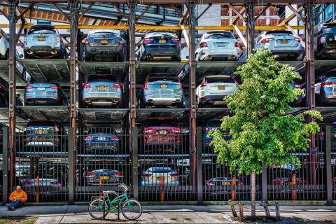 Vertikaler Parkplatz mit mehreren Ebenen, Autos übereinander geparkt, zwei Männer und ein Fahrrad vorne.