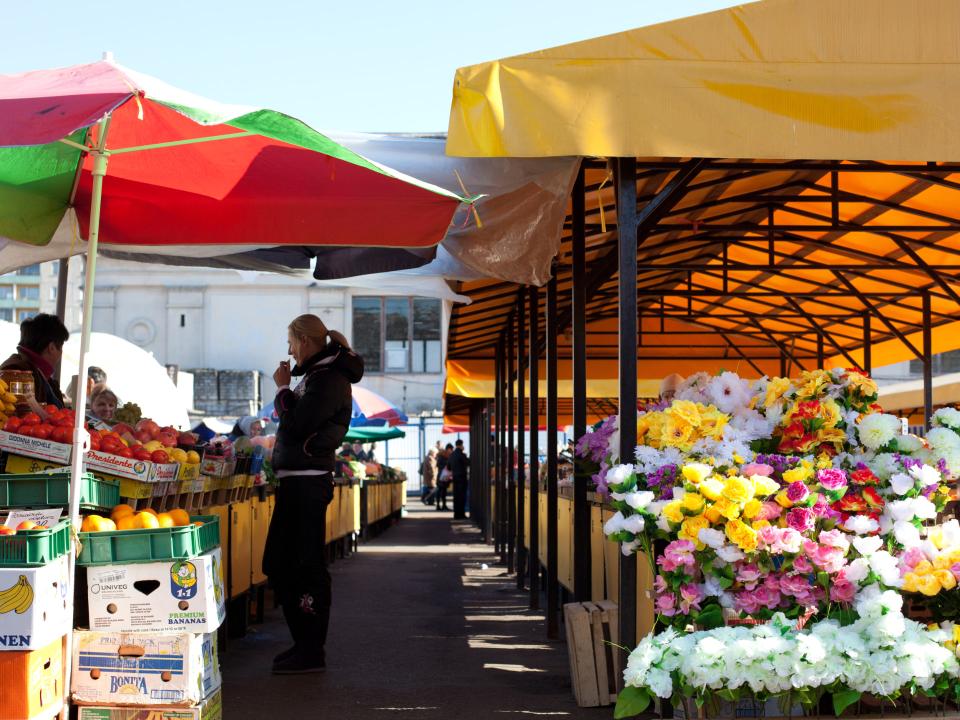 Bunter Marktstand in Vilnius mit Obst, Gemüse und Blumen unter leuchtenden Markisen.____