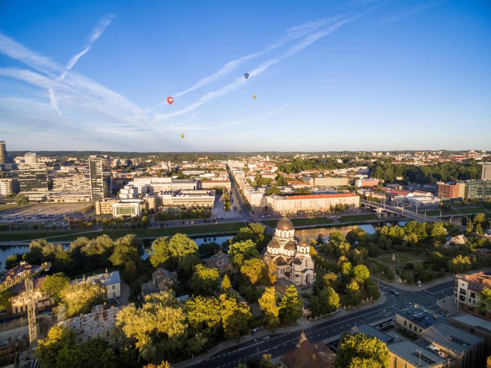 Panoramablick über Vilnius mit modernen Gebäuden, Fluss und Heißluftballons am Himmel.____