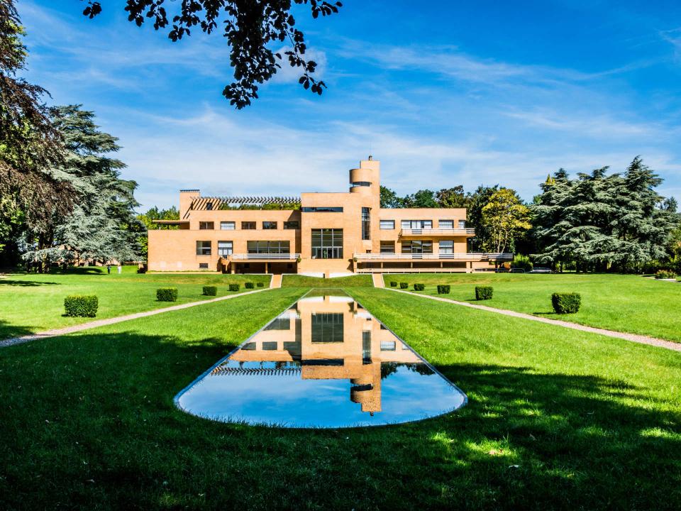 Modernes Gebäude mit großen Fenstern, umgeben von gepflegten Gärten und einem schmalen reflektierenden Wasserbecken____