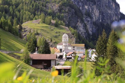 Weißer Aussichtsturm in einem idyllischen Alpendorf, eingebettet in grüne Wiesen und steile Felswände
