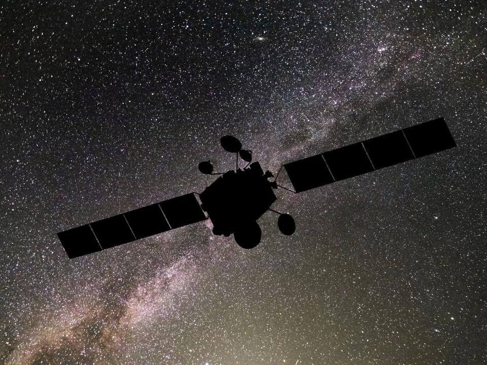 Schwarze Silhouette eines Satelliten mit Solarpanelen vor einem sternenreichen Nachthimmel.____