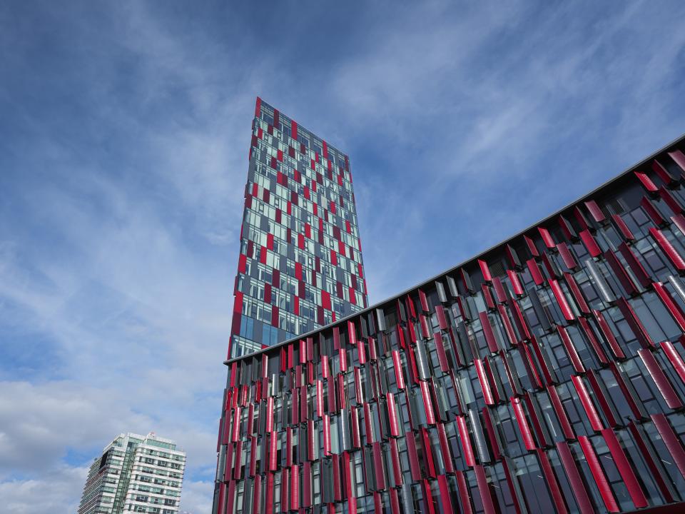 Modernes Hochhaus mit roter und schwarzer Fassadenverkleidung vor blauem Himmel, zeitgenössische Architektur.____