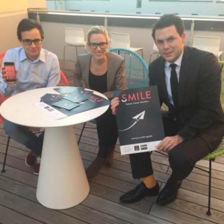 Theresa Liebherr und das Team von Smile sitzen an einem kleinen Tisch und hatten ihr Plakat hoch____