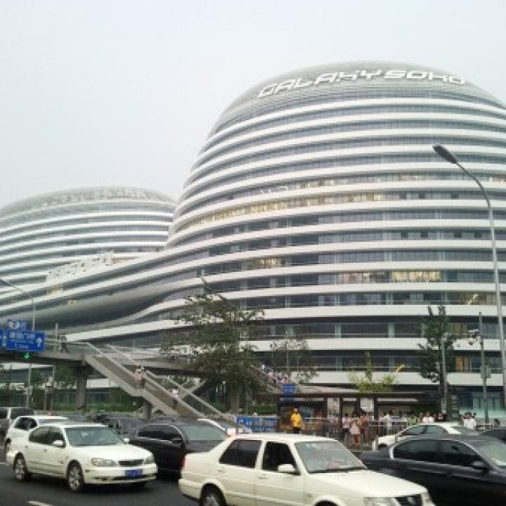 Galaxy Soho in Peking an einem nebeligen Tag. Autos fahren im Vordergrund.____