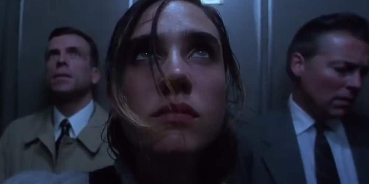 SnorriCam einer Schauspielerin im Aufzug. Ihr steht Schweiß auf der Stirn. Hinter ihr stehen zwei Männer in Anzügen.