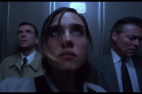 SnorriCam einer Schauspielerin im Aufzug. Ihr steht Schweiß auf der Stirn. Hinter ihr stehen zwei Männer in Anzügen.
