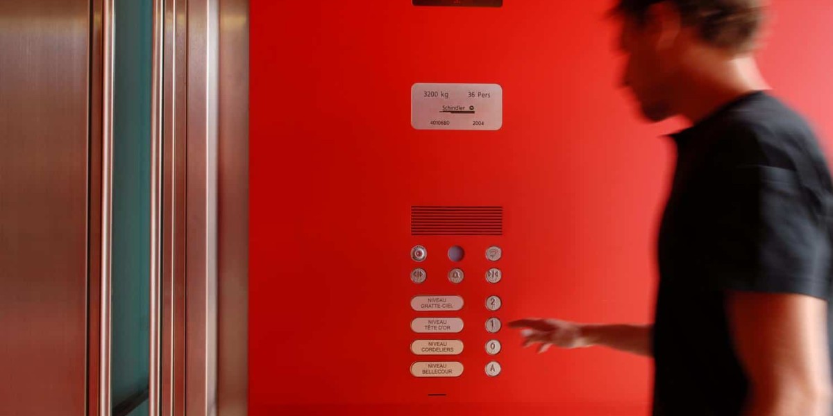 Mann betätigt Knopf eines Schindler-Fahrstuhls. Die Innenseite ist knallrot, sowie die Beschriftung der weißen Knöpfe